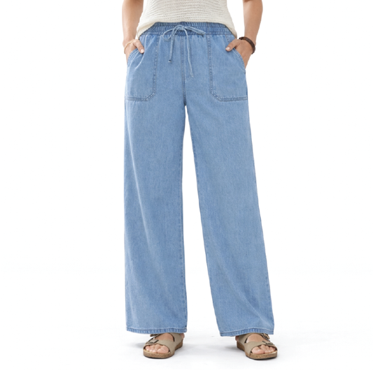 A person wearing light blue wide-leg denim pants with a drawstring waist and front patch pockets, paired with a cream top and tan sandals, shown against a plain white background.